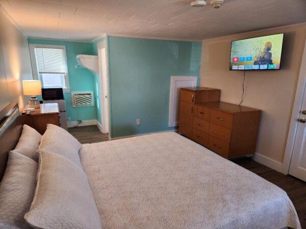 A bedroom with a bed, dresser, and TV.